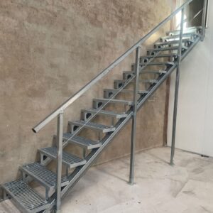 Escalera metálica StarModul recta, con peldaños de rejilla tramex y barandilla de tubo, montada en una nave